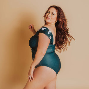 woman showing the side of her one-piece swimsuit in green and floral design