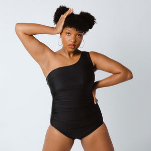 Woman poses in one piece swimsuit with one shoulder