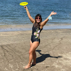 Woman standing with arms in the air wearing a black one-piece swimsuit 